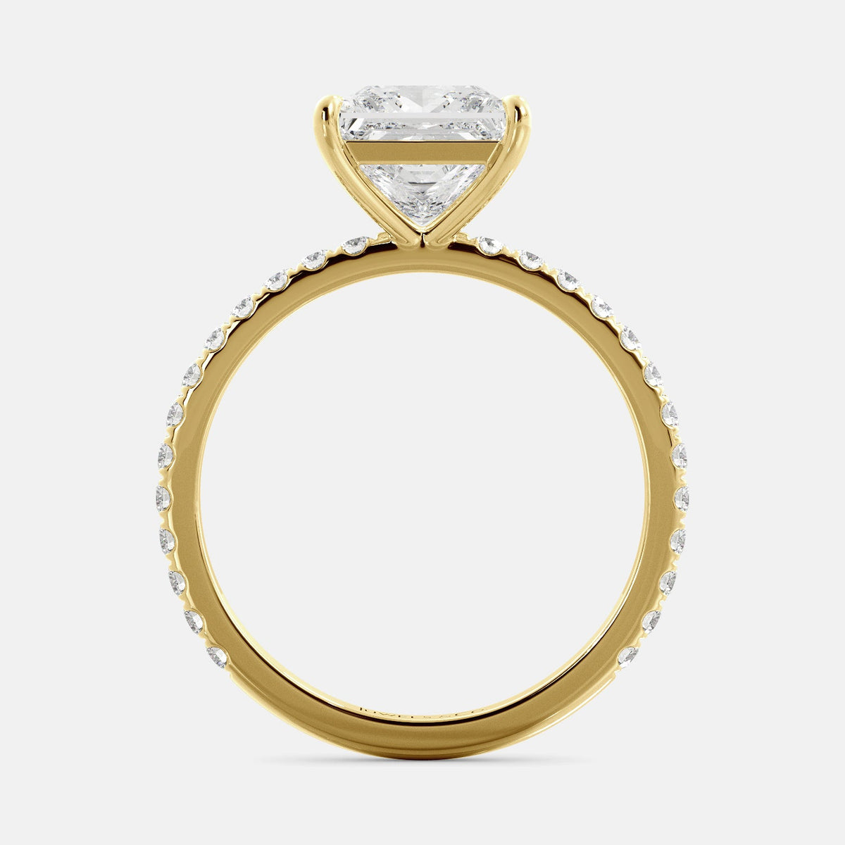 A close-up of a yellow gold cushion solitaire lab-grown diamond ring with an eternity band. The lab-grown diamond is a climate -positive diamond, created by using carbon from the atmosphere. The ring is set with a 1-carat cushion-cut diamond in the center, surrounded by a row of smaller diamonds on the band. The ring is available in a variety of sizes and starts at \\$6,400.00.