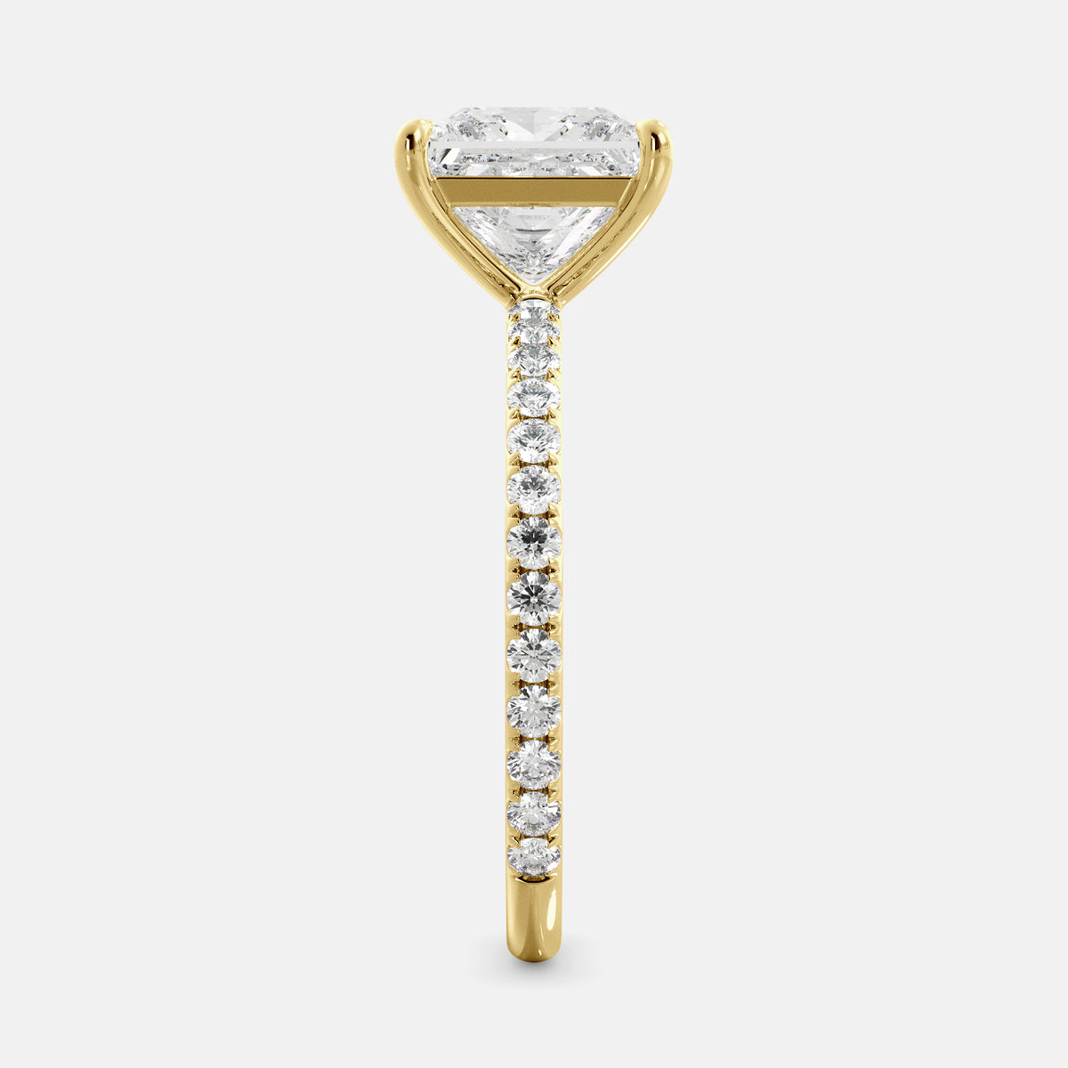 A close-up of a yellow gold cushion solitaire lab-grown diamond ring with an eternity band. The lab-grown diamond is a climate -positive diamond, created by using carbon from the atmosphere. The ring is set with a 1-carat cushion-cut diamond in the center, surrounded by a row of smaller diamonds on the band. The ring is available in a variety of sizes and starts at \\$6,400.00.