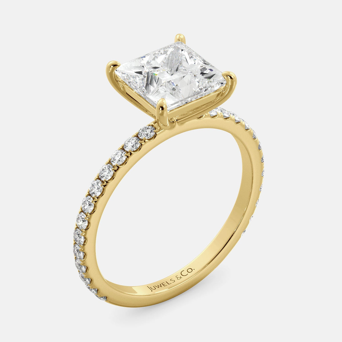 A close-up of a yellow gold cushion solitaire lab-grown diamond ring with an eternity band. The lab-grown diamond is a climate -positive diamond, created by using carbon from the atmosphere. The ring is set with a 1-carat cushion-cut diamond in the center, surrounded by a row of smaller diamonds on the band. The ring is available in a variety of sizes and starts at \\$6,400.00.