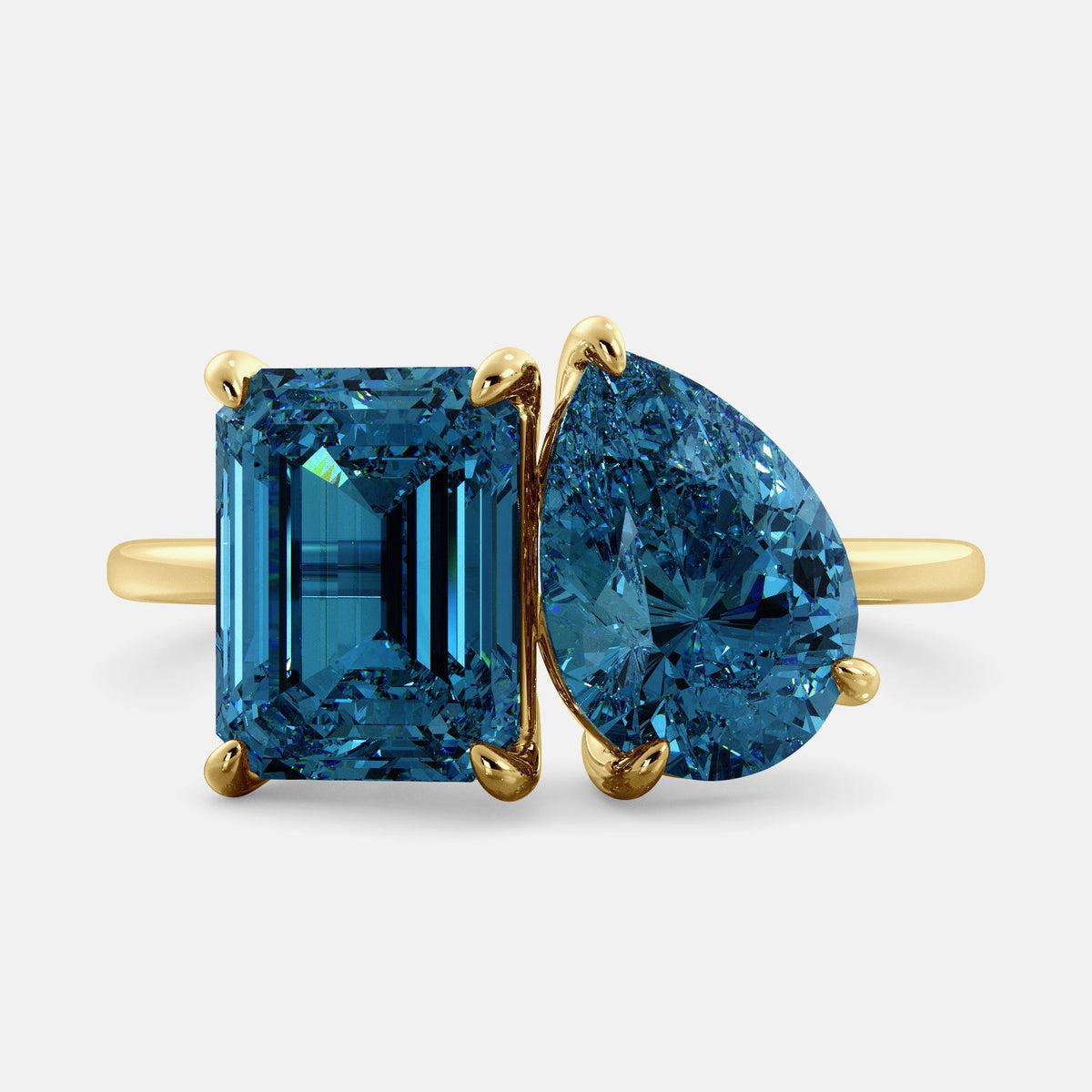 A toi et moi ring with two london blue topaz gemstones. The first gemstone is an emerald cut, and the second gemstone is a pear shape. The ring is made of 14k yellow gold and is set on a dainty band. The gemstones are sparkling in the light and are a beautiful and meaningful piece of jewelry.