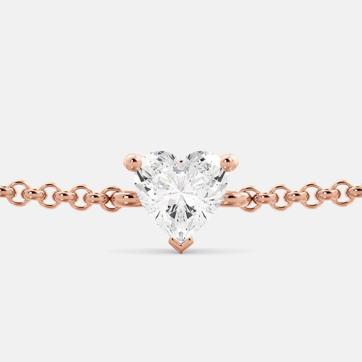 A close-up of a heart-shaped diamond bracelet in recycled rose gold. The bracelet is set with a single, large diamond in the center of a heart-shaped pendant. The bracelet is made of recycled rose gold and has a simple, elegant design. The diamond is sparkling and reflects light beautifully. The bracelet is a perfect gift for a loved one or a special occasion.