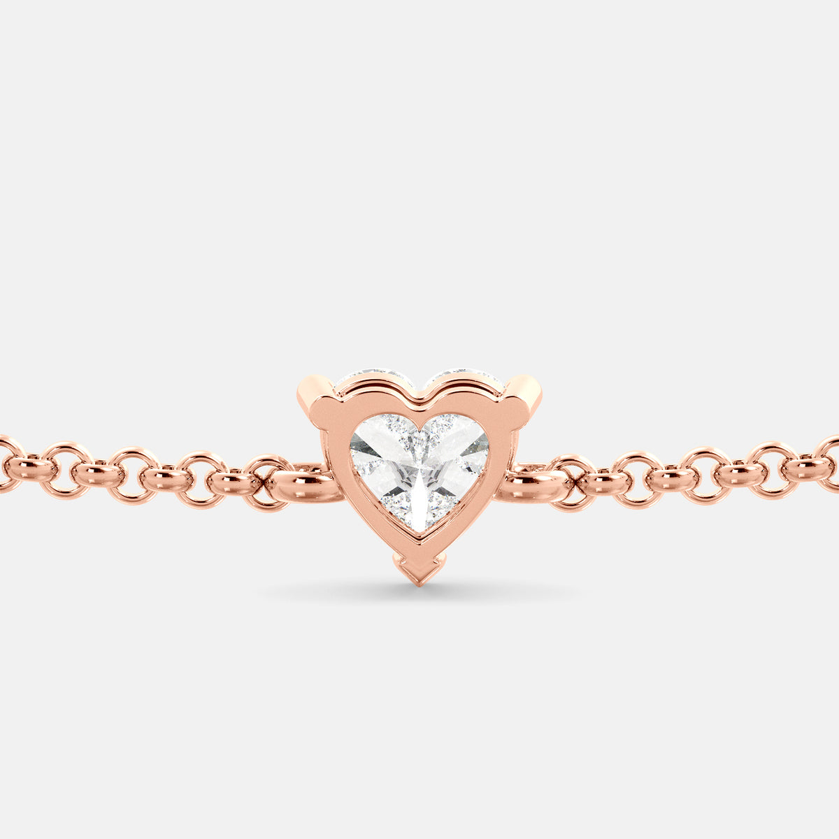 A close-up of a heart-shaped diamond bracelet in recycled rose gold. The bracelet is set with a single, large diamond in the center of a heart-shaped pendant. The bracelet is made of recycled rose gold and has a simple, elegant design. The diamond is sparkling and reflects light beautifully. The bracelet is a perfect gift for a loved one or a special occasion.
