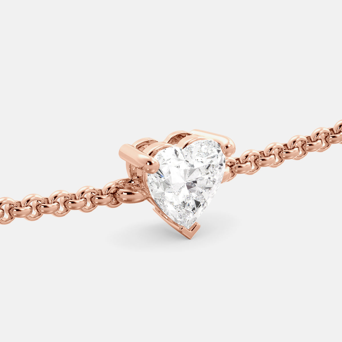 A close-up of a heart-shaped diamond bracelet in recycled rose gold. The bracelet is set with a single, large diamond in the center of a heart-shaped pendant. The bracelet is made of recycled rose gold and has a simple, elegant design. The diamond is sparkling and reflects light beautifully. The bracelet is a perfect gift for a loved one or a special occasion.