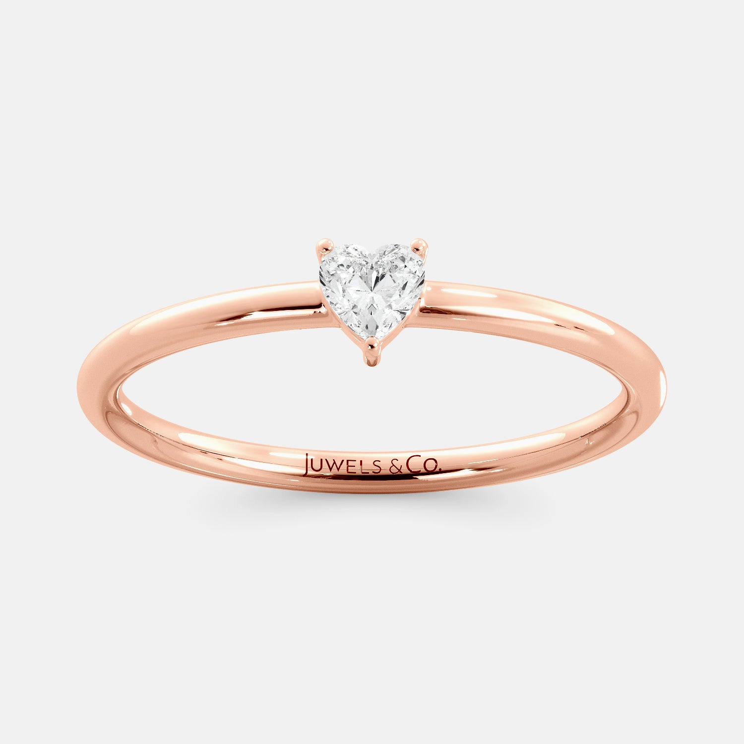 A close-up of a heart-shaped solitaire diamond ring in recycled rose gold. The ring is set with a single, large diamond in the center of a heart-shaped setting. The ring is made of recycled rose gold and has a simple, elegant design. The diamond is sparkling and reflects light beautifully. The ring is a perfect gift for a loved one or a special occasion.