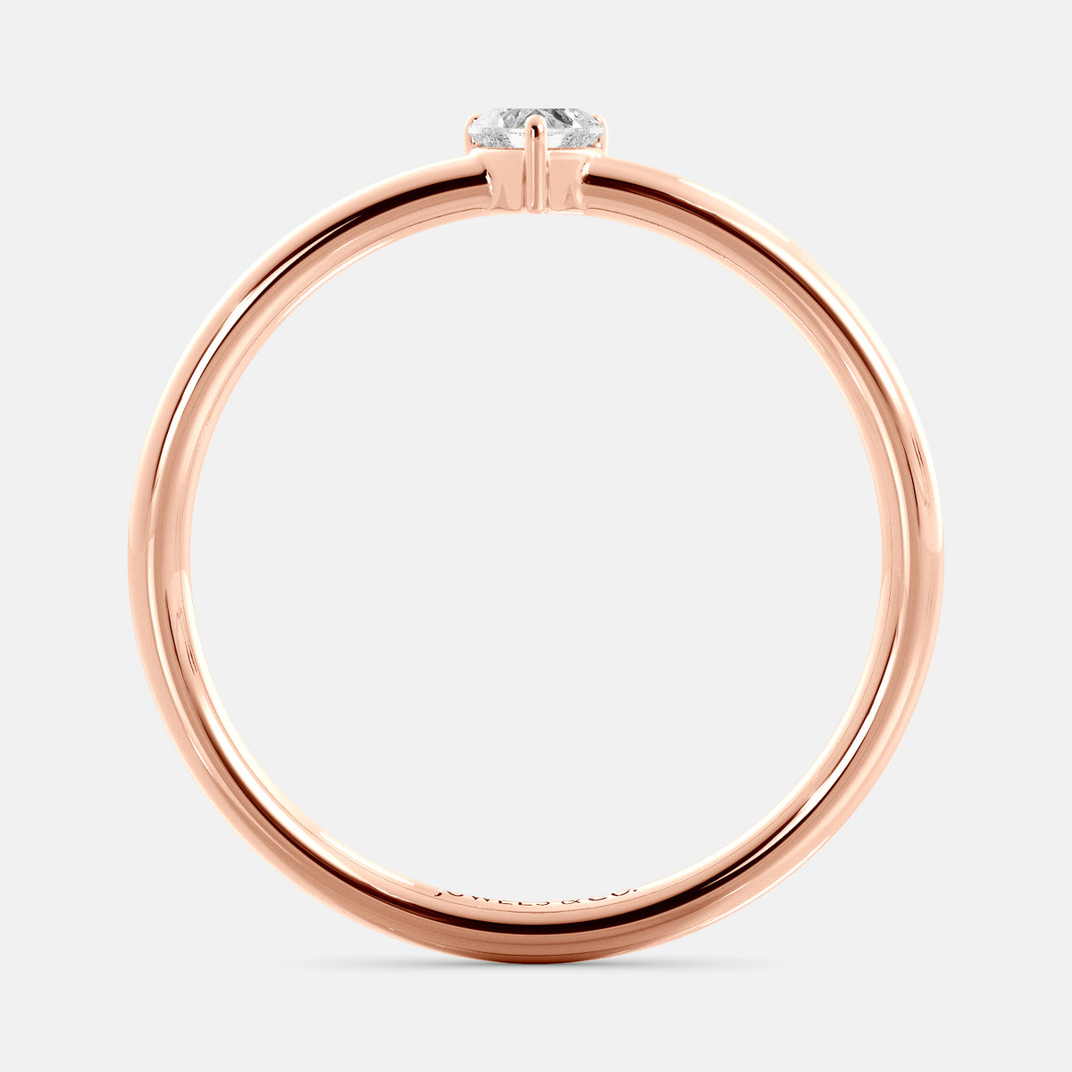 A close-up of a heart-shaped solitaire diamond ring in recycled rose gold. The ring is set with a single, large diamond in the center of a heart-shaped setting. The ring is made of recycled rose gold and has a simple, elegant design. The diamond is sparkling and reflects light beautifully. The ring is a perfect gift for a loved one or a special occasion.