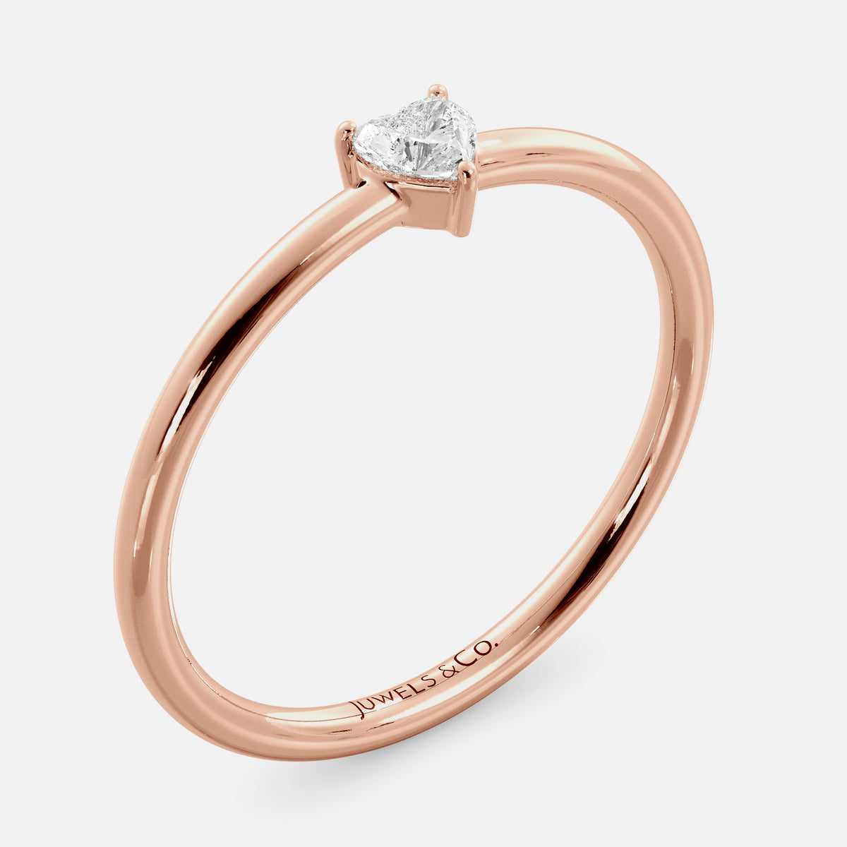 A close-up of a heart-shaped solitaire diamond ring in recycled rose gold. The ring is set with a single, large diamond in the center of a heart-shaped setting. The ring is made of recycled rose gold and has a simple, elegant design. The diamond is sparkling and reflects light beautifully. The ring is a perfect gift for a loved one or a special occasion.