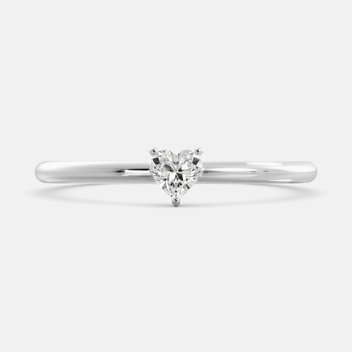 A close-up of a heart-shaped solitaire diamond ring in recycled white gold. The ring is set with a single, large diamond in the center of a heart-shaped setting. The ring is made of recycled white gold and has a simple, elegant design. The diamond is sparkling and reflects light beautifully. The ring is a perfect gift for a loved one or a special occasion.