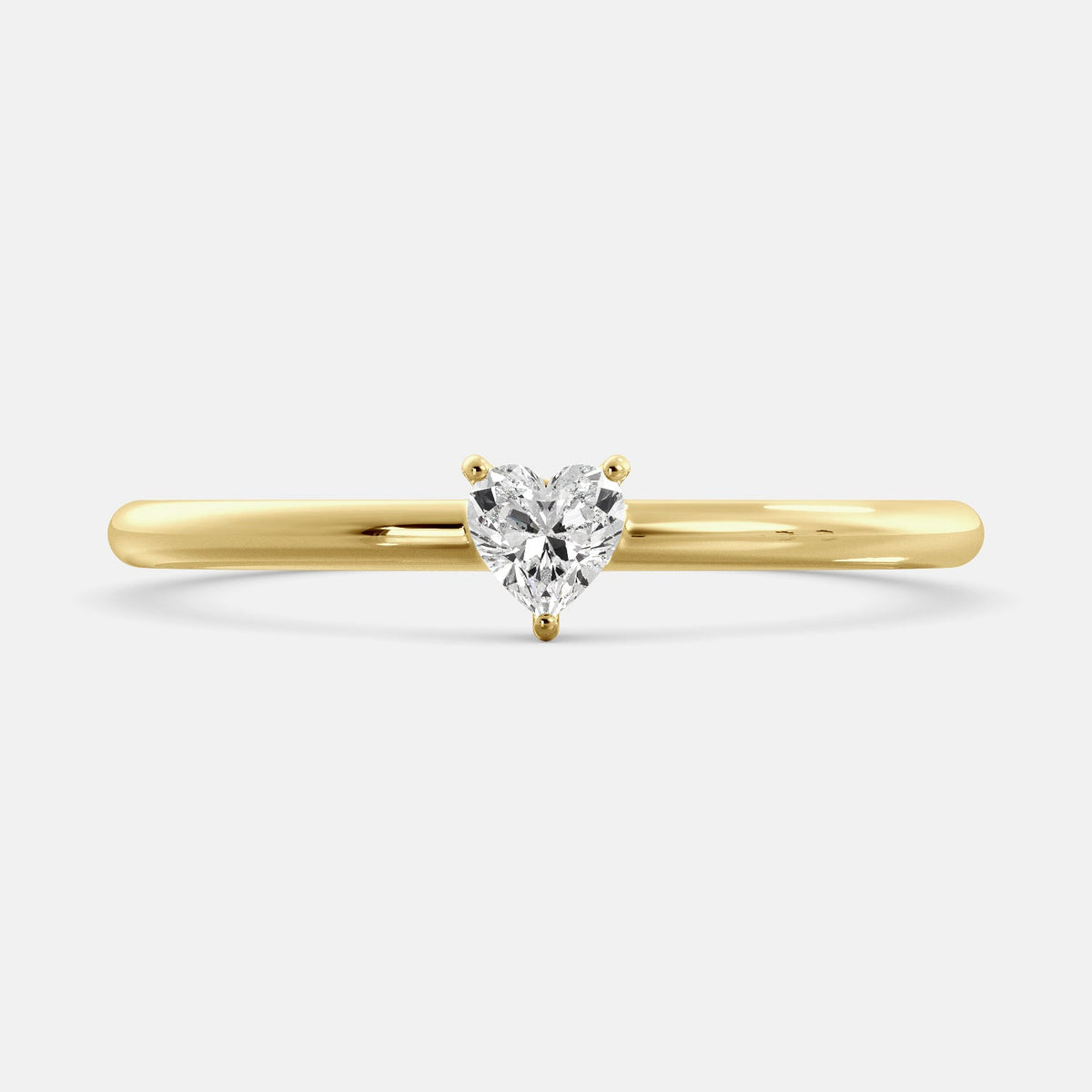 A close-up of a heart-shaped solitaire diamond ring in recycled yellow gold. The ring is set with a single, large diamond in the center of a heart-shaped setting. The ring is made of recycled yellow gold and has a simple, elegant design. The diamond is sparkling and reflects light beautifully. The ring is a perfect gift for a loved one or a special occasion.