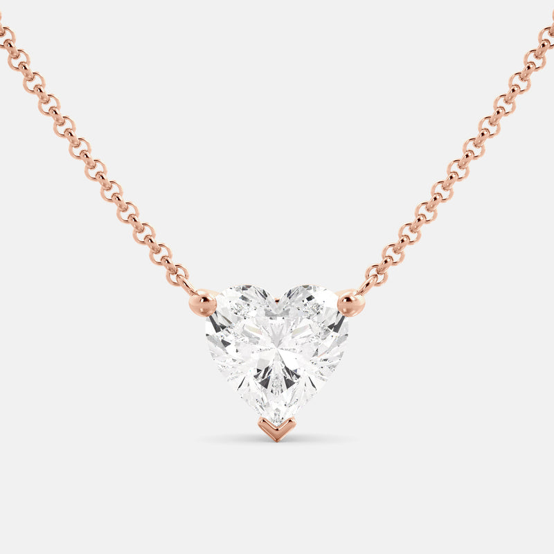 A close-up of a heart-shaped diamond necklace in recycled rose gold. The necklace is set with a single heart-shaped diamond in the center of a pendant. The necklace is made of recycled rose gold and has a simple, elegant design. The diamond is sparkling and reflects light beautifully. The necklace is a perfect gift for a loved one or a special occasion.