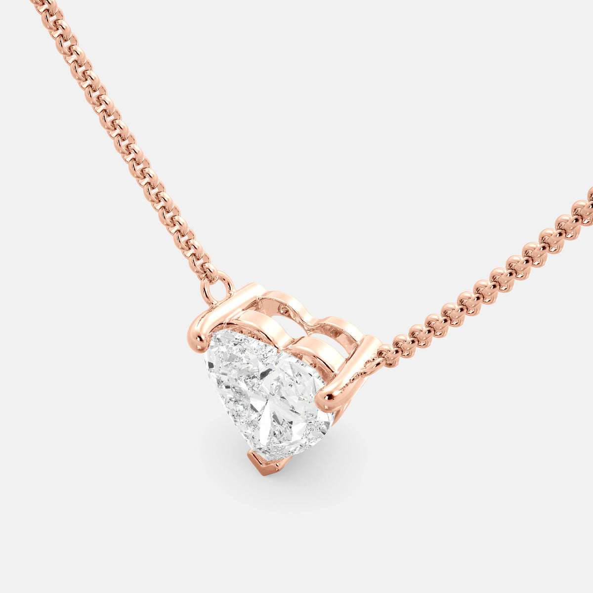 A close-up of a heart-shaped diamond necklace in recycled rose gold. The necklace is set with a single heart-shaped diamond in the center of a pendant. The necklace is made of recycled rose gold and has a simple, elegant design. The diamond is sparkling and reflects light beautifully. The necklace is a perfect gift for a loved one or a special occasion.