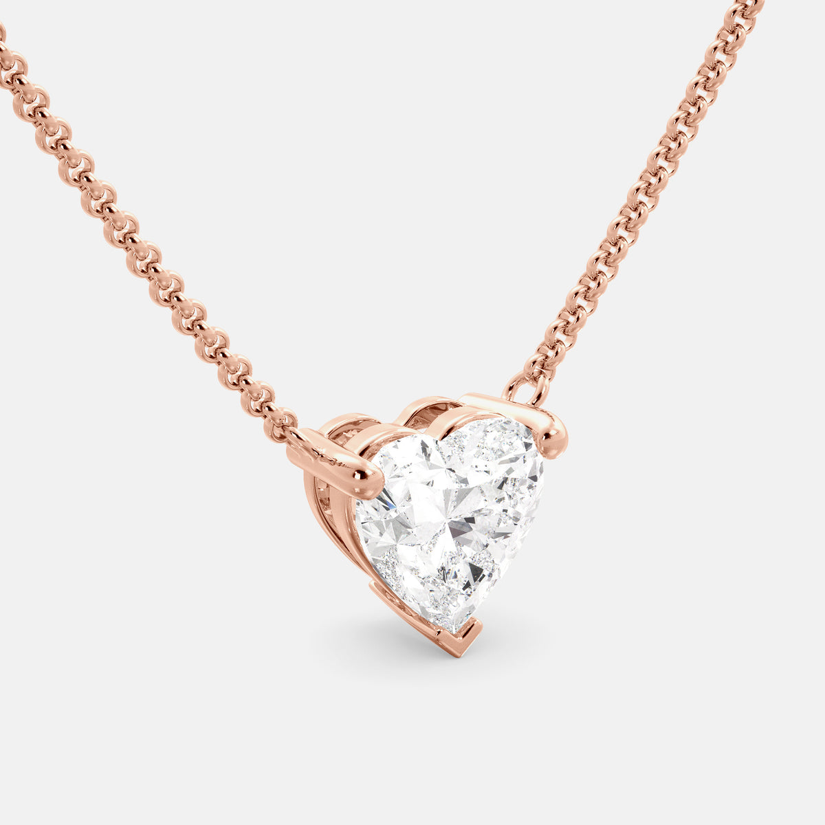 A close-up of a heart-shaped diamond necklace in recycled rose gold. The necklace is set with a single heart-shaped diamond in the center of a pendant. The necklace is made of recycled rose gold and has a simple, elegant design. The diamond is sparkling and reflects light beautifully. The necklace is a perfect gift for a loved one or a special occasion.