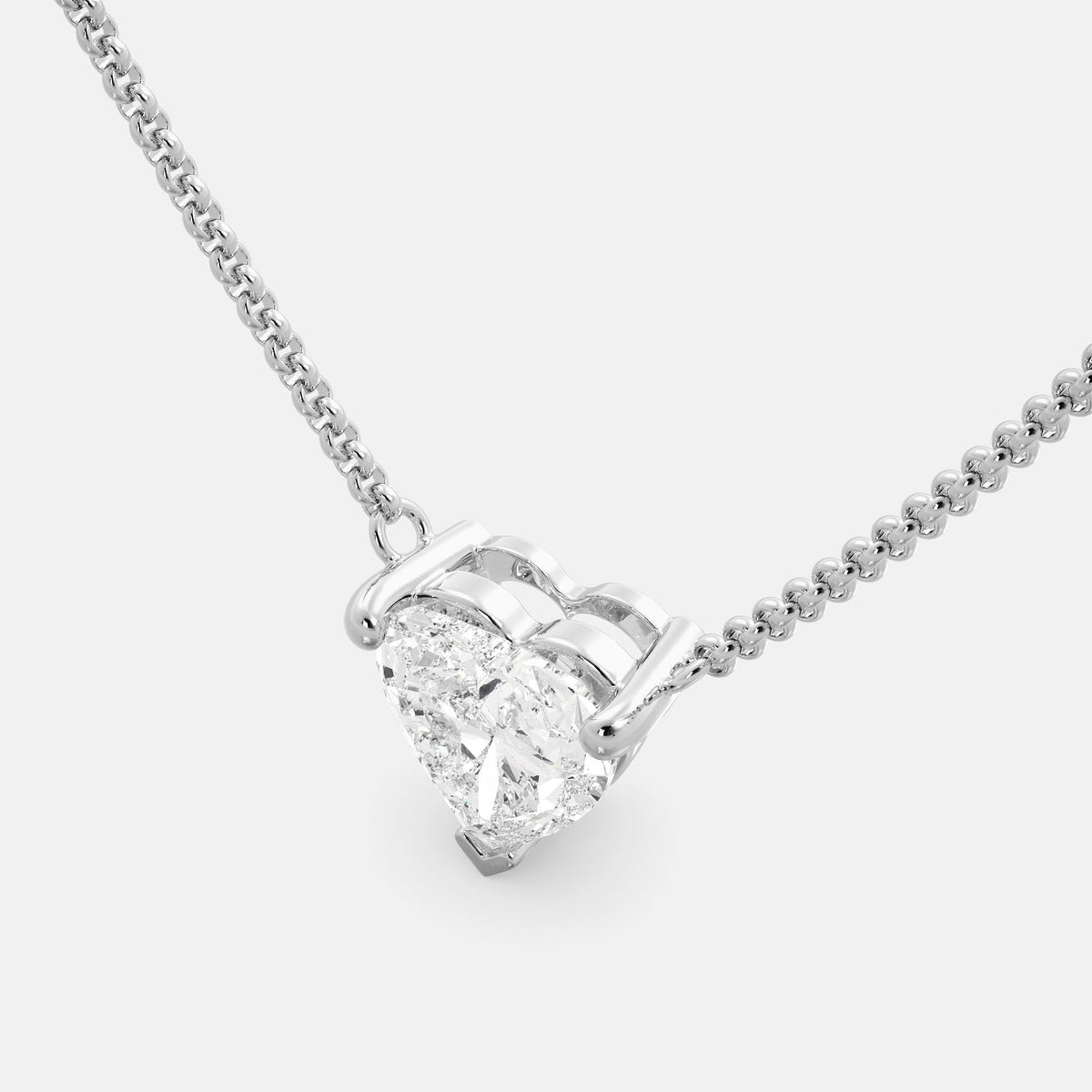 A close-up of a heart-shaped diamond necklace in recycled white gold. The necklace is set with a single heart-shaped diamond in the center of a pendant. The necklace is made of recycled white gold and has a simple, elegant design. The diamond is sparkling and reflects light beautifully. The necklace is a perfect gift for a loved one or a special occasion.