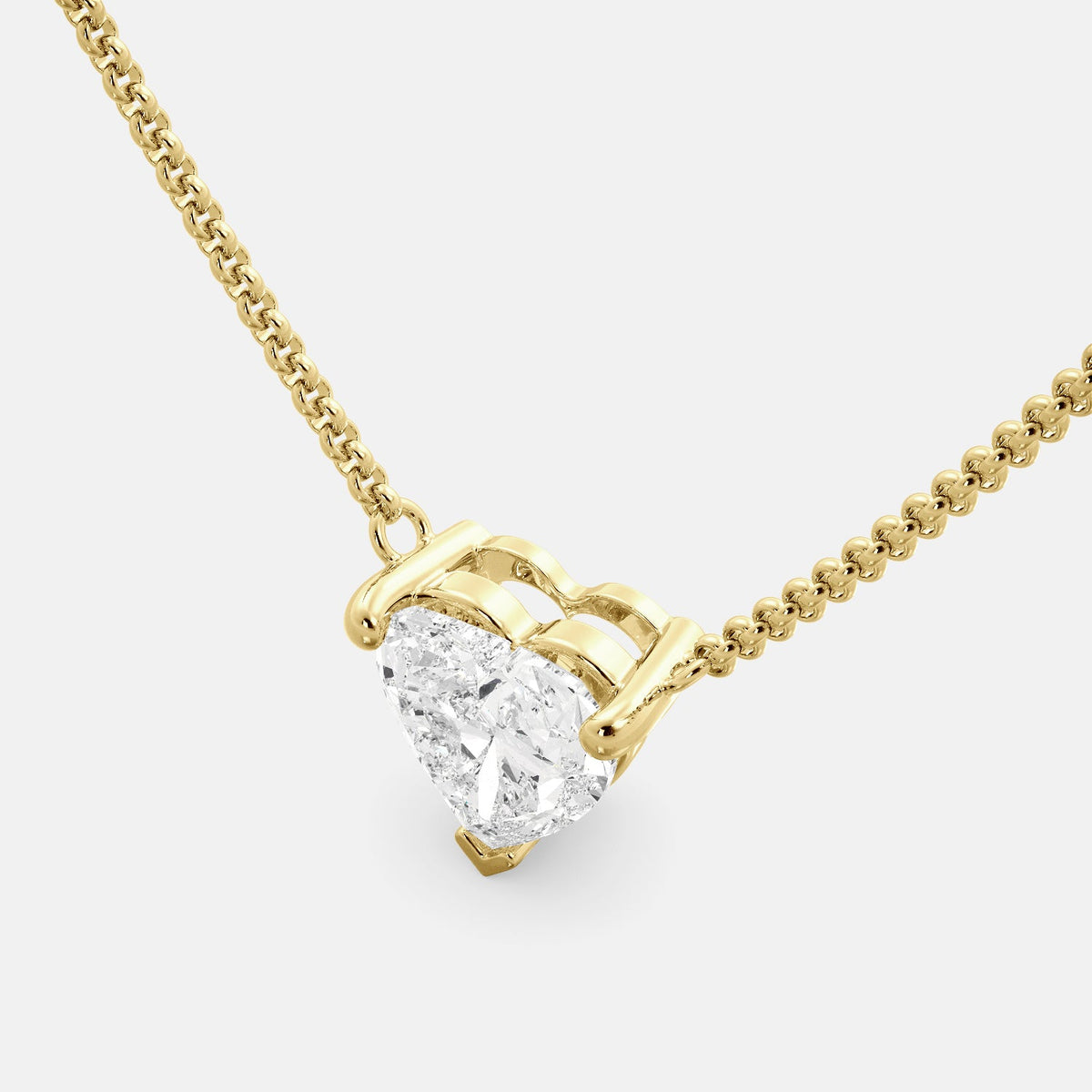 A close-up of a heart-shaped diamond necklace in recycled yellow gold. The necklace is set with a single heart-shaped diamond in the center of a pendant. The necklace is made of recycled yellow gold and has a simple, elegant design. The diamond is sparkling and reflects light beautifully. The necklace is a perfect gift for a loved one or a special occasion.
