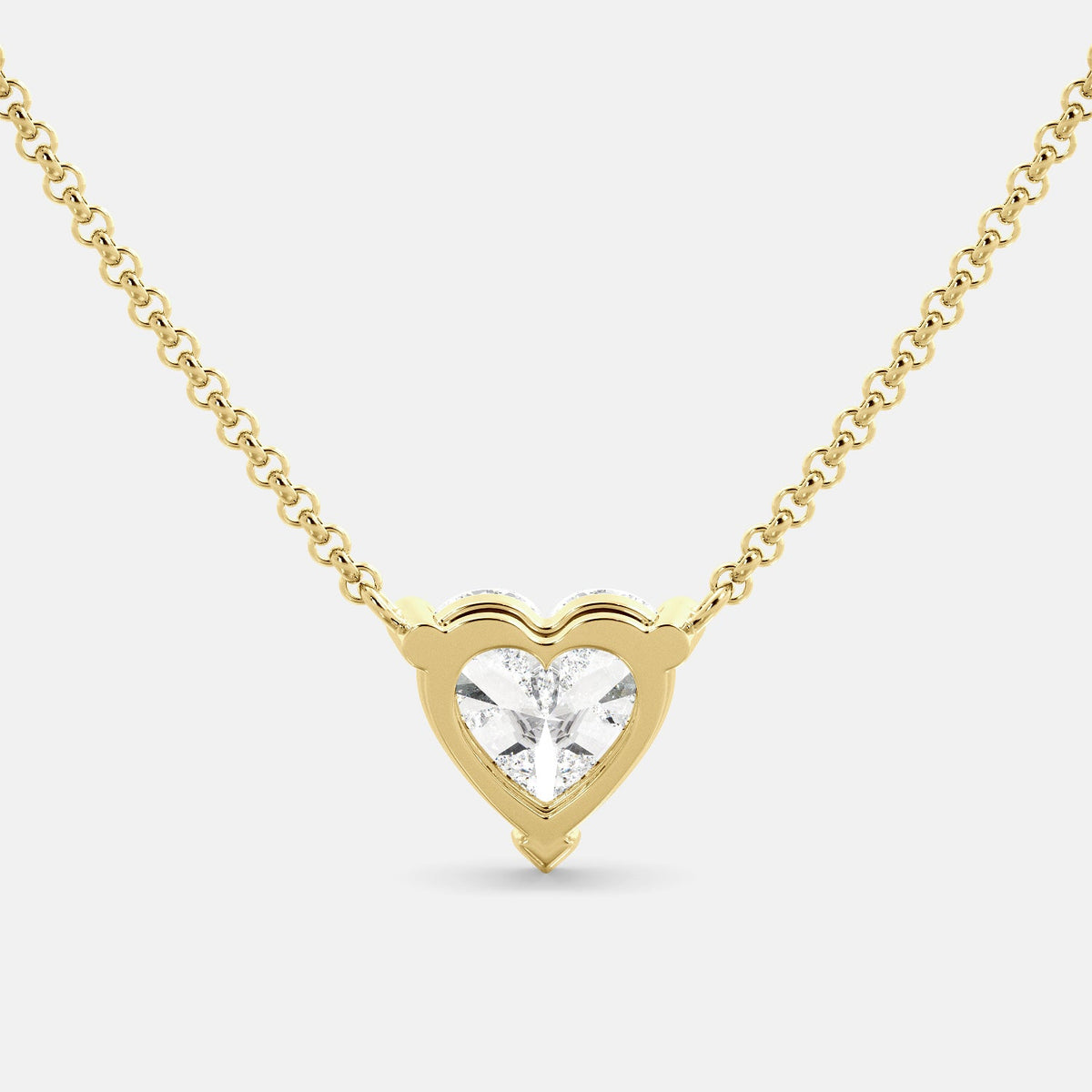 A close-up of a heart-shaped diamond necklace in recycled yellow gold. The necklace is set with a single heart-shaped diamond in the center of a pendant. The necklace is made of recycled yellow gold and has a simple, elegant design. The diamond is sparkling and reflects light beautifully. The necklace is a perfect gift for a loved one or a special occasion.