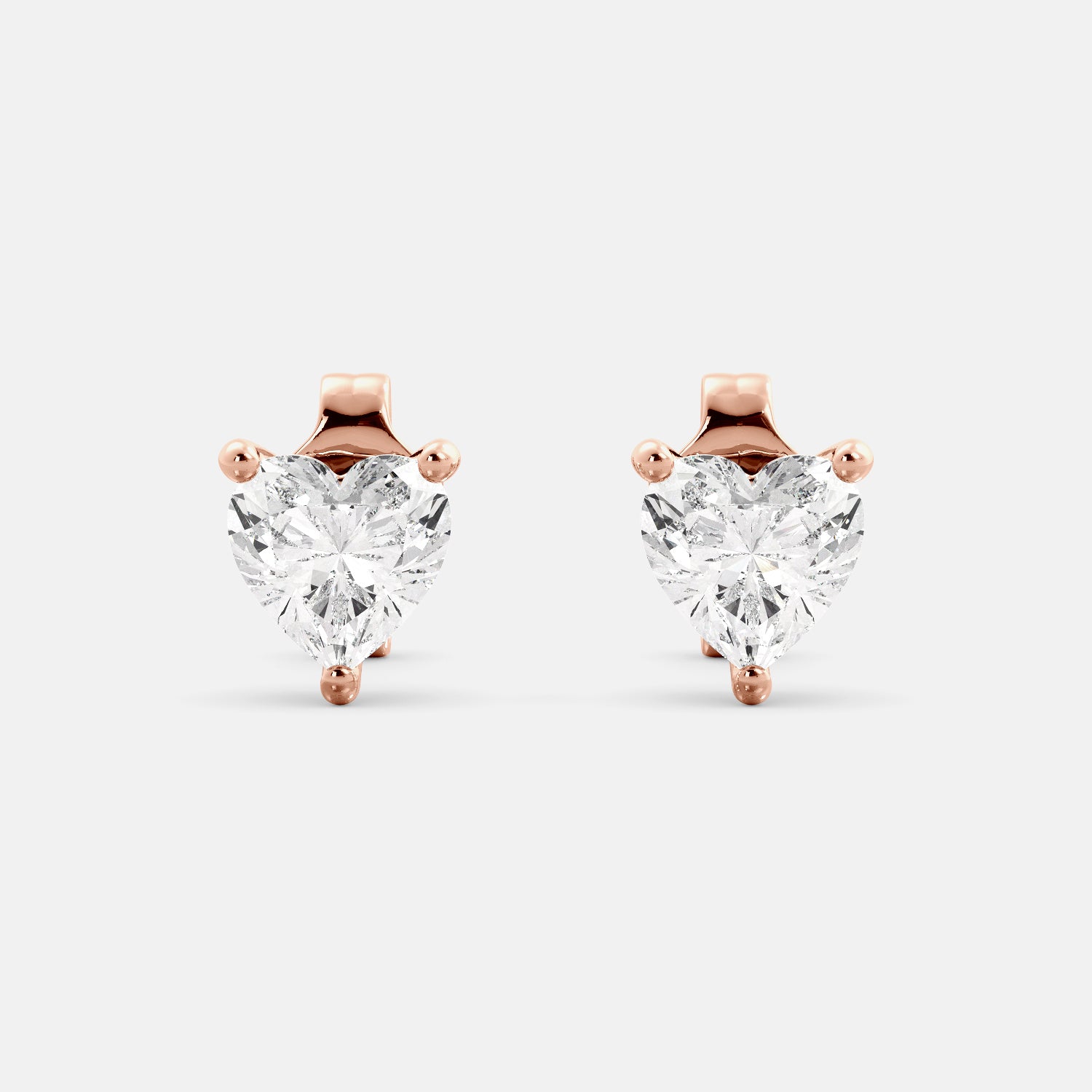 A close-up of a pair of heart-shaped diamond stud earrings in recycled rose gold. Each earring is set with a single heart shape diamond in the center. The earrings are made of recycled rose gold and have a simple, elegant design. The diamonds are sparkling and reflect light beautifully. The earrings are a perfect gift for a loved one or a special occasion.