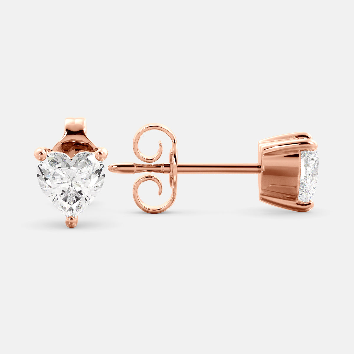 A close-up of a pair of heart-shaped diamond stud earrings in recycled rose gold. Each earring is set with a single heart shape diamond in the center. The earrings are made of recycled rose gold and have a simple, elegant design. The diamonds are sparkling and reflect light beautifully. The earrings are a perfect gift for a loved one or a special occasion.