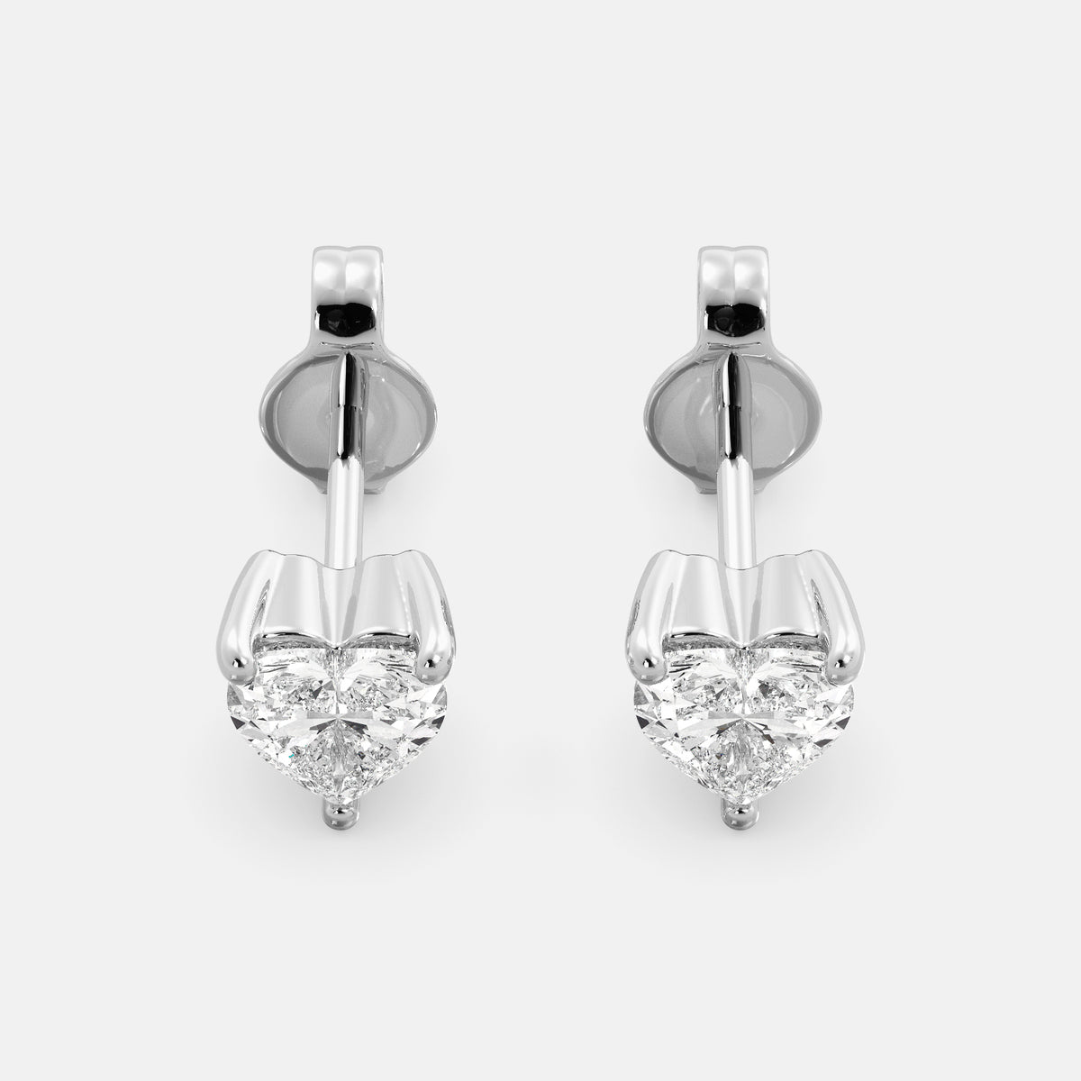 A close-up of a pair of heart-shaped diamond stud earrings in recycled white gold. Each earring is set with a single heart shape diamond in the center. The earrings are made of recycled white gold and have a simple, elegant design. The diamonds are sparkling and reflect light beautifully. The earrings are a perfect gift for a loved one or a special occasion.