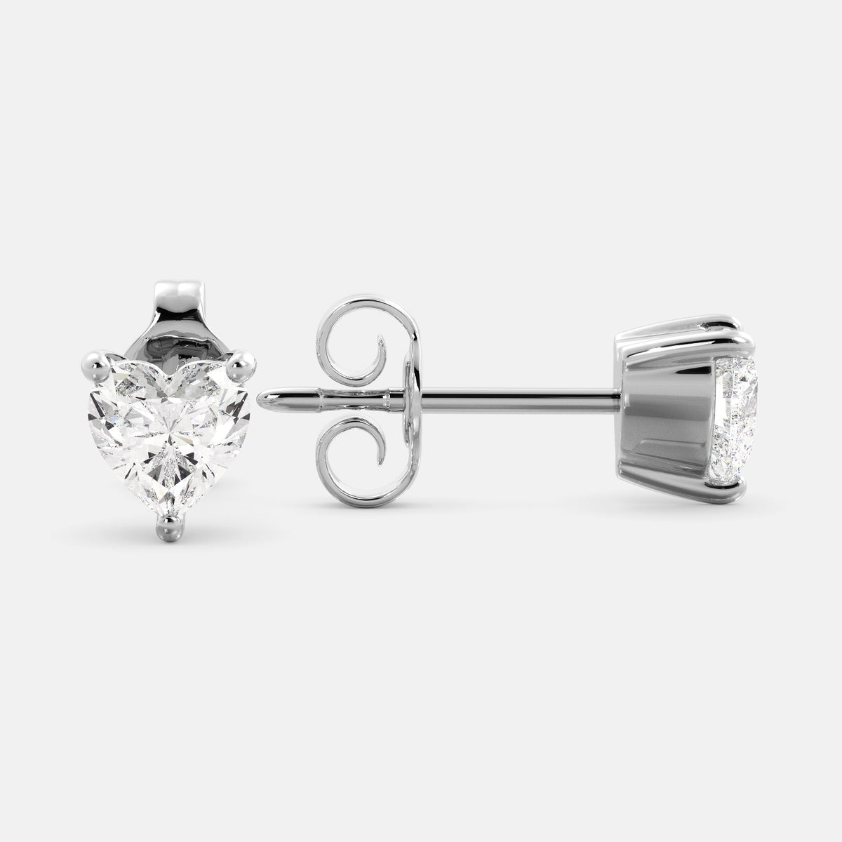 A close-up of a pair of heart-shaped diamond stud earrings in recycled white gold. Each earring is set with a single heart shape diamond in the center. The earrings are made of recycled white gold and have a simple, elegant design. The diamonds are sparkling and reflect light beautifully. The earrings are a perfect gift for a loved one or a special occasion.