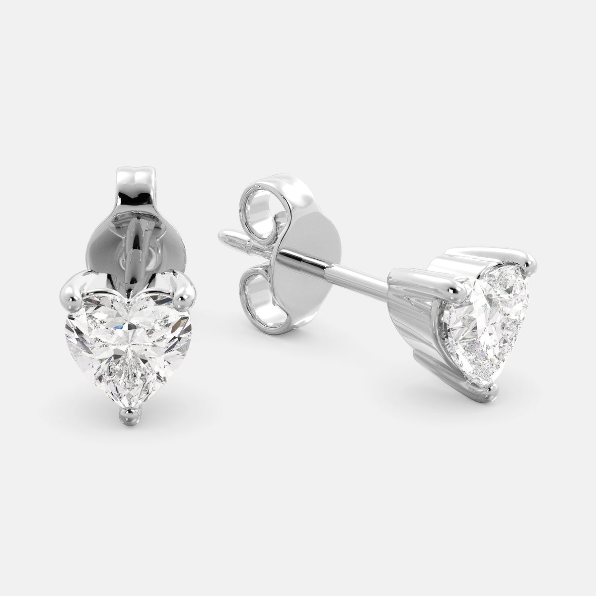 A close-up of a pair of heart-shaped diamond stud earrings in recycled white gold. Each earring is set with a single heart shape diamond in the center. The earrings are made of recycled white gold and have a simple, elegant design. The diamonds are sparkling and reflect light beautifully. The earrings are a perfect gift for a loved one or a special occasion.