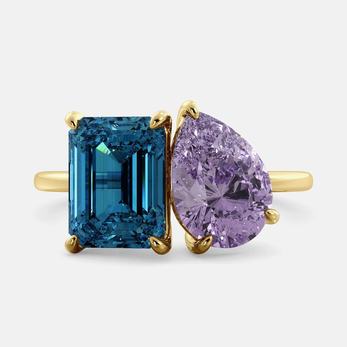 A toi et moi ring with an emerald-cut London Blue Topaz and pear-cut gemstone. The emerald-cut is set on the left of the ring, and the pear-cut gemstone is set on the right. The ring is made of recycled yellow gold and has a simple, elegant design. The pear-cut gemstone can be customized. **Here are some additional details about the image:** * The emerald-cut white London Blue Topaz is a birthstone for December. * The pear-cut gemstone can be customized to any stone of your choice.