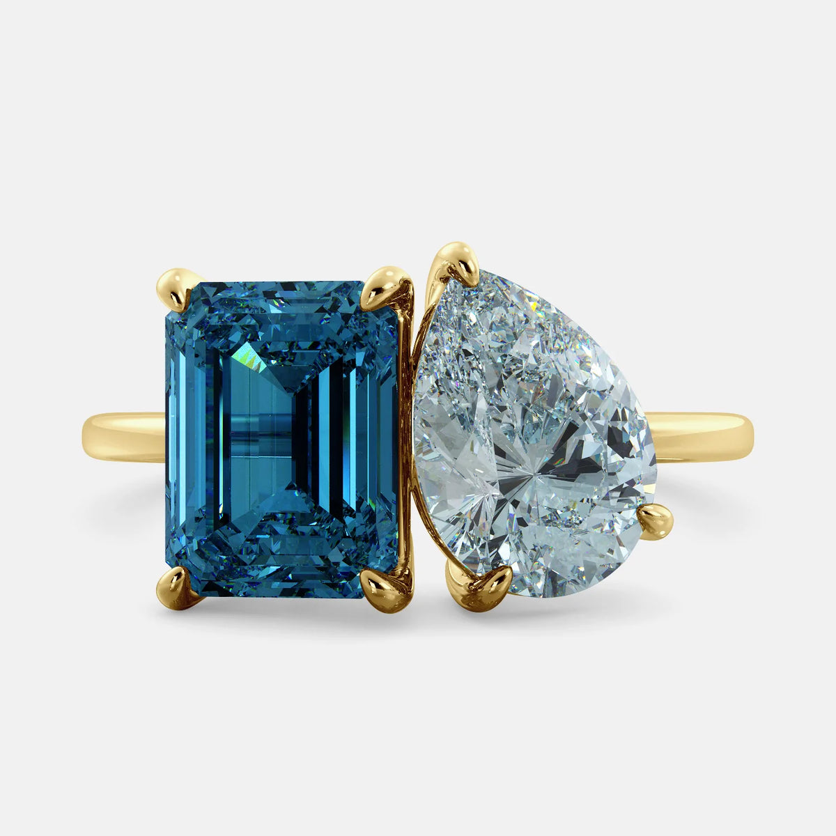 A toi et moi ring with an emerald-cut London Blue Topaz and pear-cut gemstone. The emerald-cut morganite is set on the left of the ring, and the pear-cut gemstone is set on the right. The ring is made of recycled yellow gold and has a simple, elegant design. The pear-cut gemstone can be customized. **Here are some additional details about the image:** * The emerald-cut white London Blue Topaz is a birthstone for December. * The pear-cut gemstone can be customized to any stone of your choice.