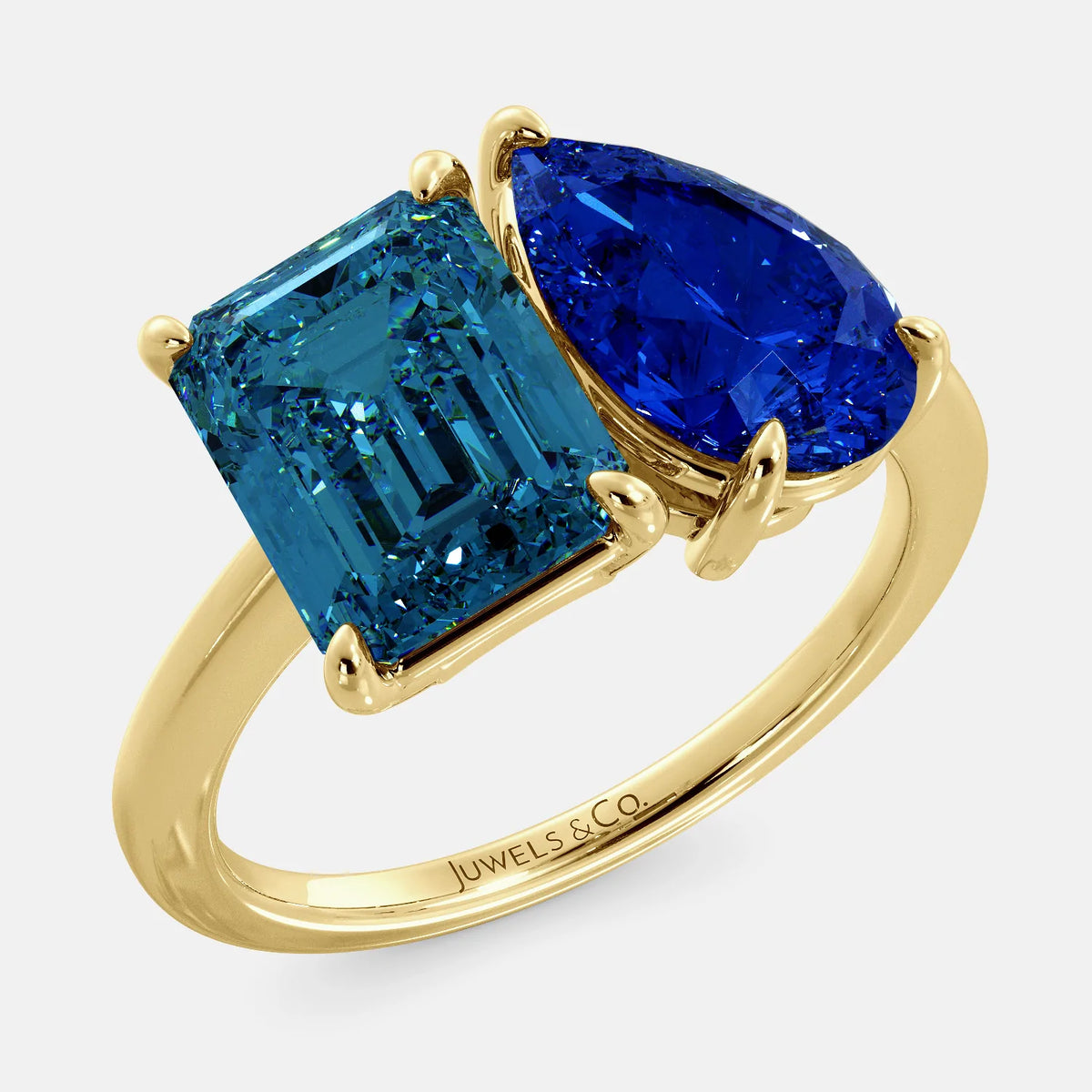 A toi et moi ring with an emerald-cut London Blue Topaz and pear-cut gemstone. The emerald-cut morganite is set on the left of the ring, and the pear-cut gemstone is set on the right. The ring is made of recycled yellow gold and has a simple, elegant design. The pear-cut gemstone can be customized. **Here are some additional details about the image:** * The emerald-cut white London Blue Topaz is a birthstone for December. * The pear-cut gemstone can be customized to any stone of your choice.
