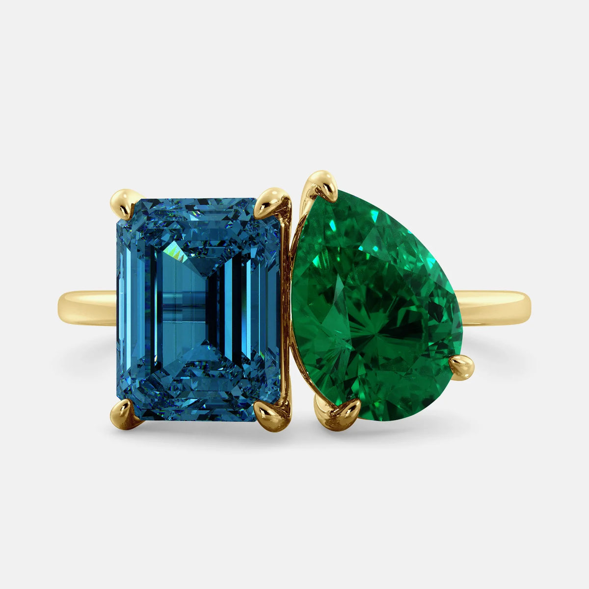 A toi et moi ring with an emerald-cut London Blue Topaz and pear-cut gemstone. The emerald-cut morganite is set on the left of the ring, and the pear-cut gemstone is set on the right. The ring is made of recycled yellow gold and has a simple, elegant design. The pear-cut gemstone can be customized. **Here are some additional details about the image:** * The emerald-cut white London Blue Topaz is a birthstone for December. * The pear-cut gemstone can be customized to any stone of your choice.