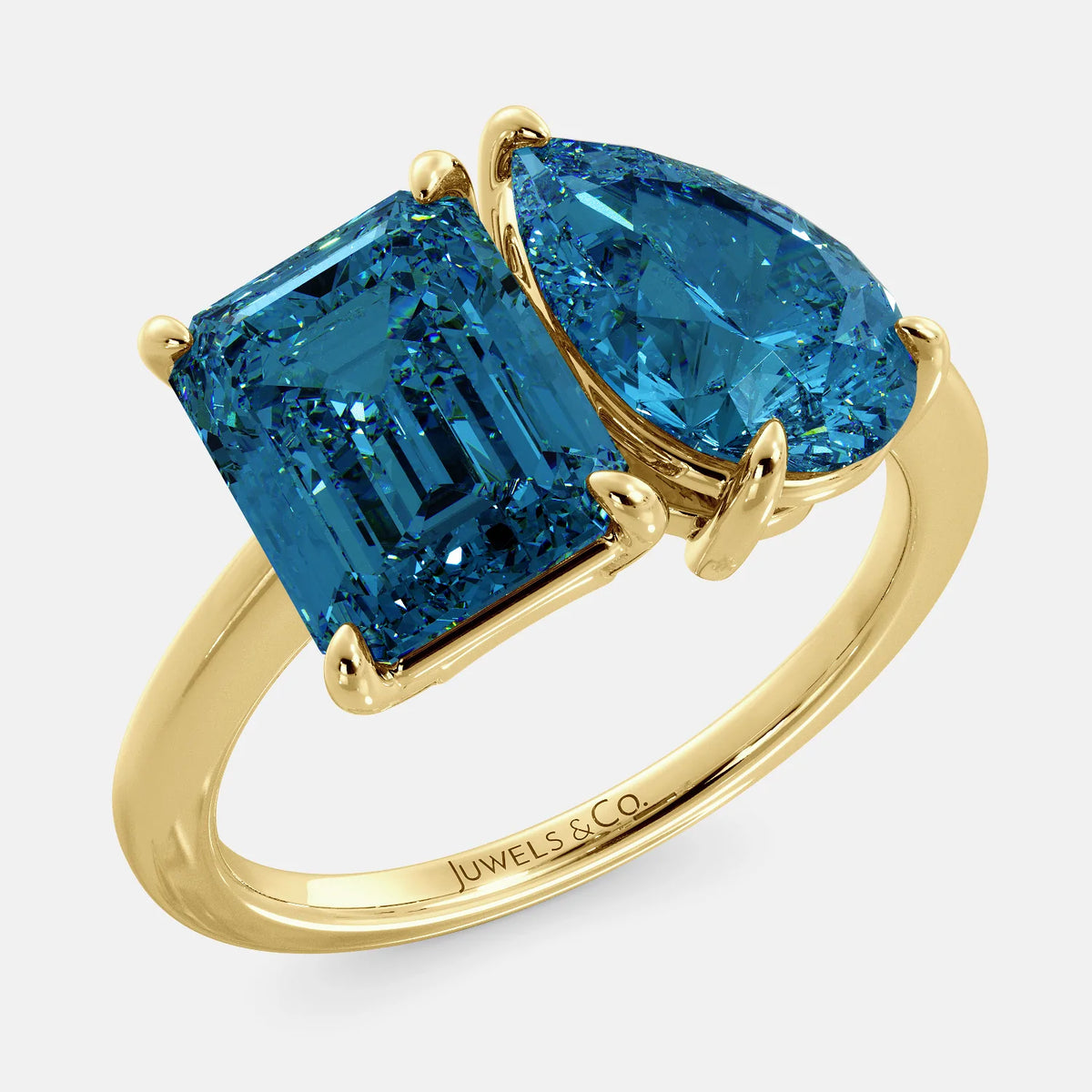 A toi et moi ring with an emerald-cut London Blue Topaz and pear-cut gemstone. The emerald-cut morganite is set on the left of the ring, and the pear-cut gemstone is set on the right. The ring is made of recycled yellow gold and has a simple, elegant design. The pear-cut gemstone can be customized. **Here are some additional details about the image:** * The emerald-cut white London Blue Topaz is a birthstone for December. * The pear-cut gemstone can be customized to any stone of your choice.