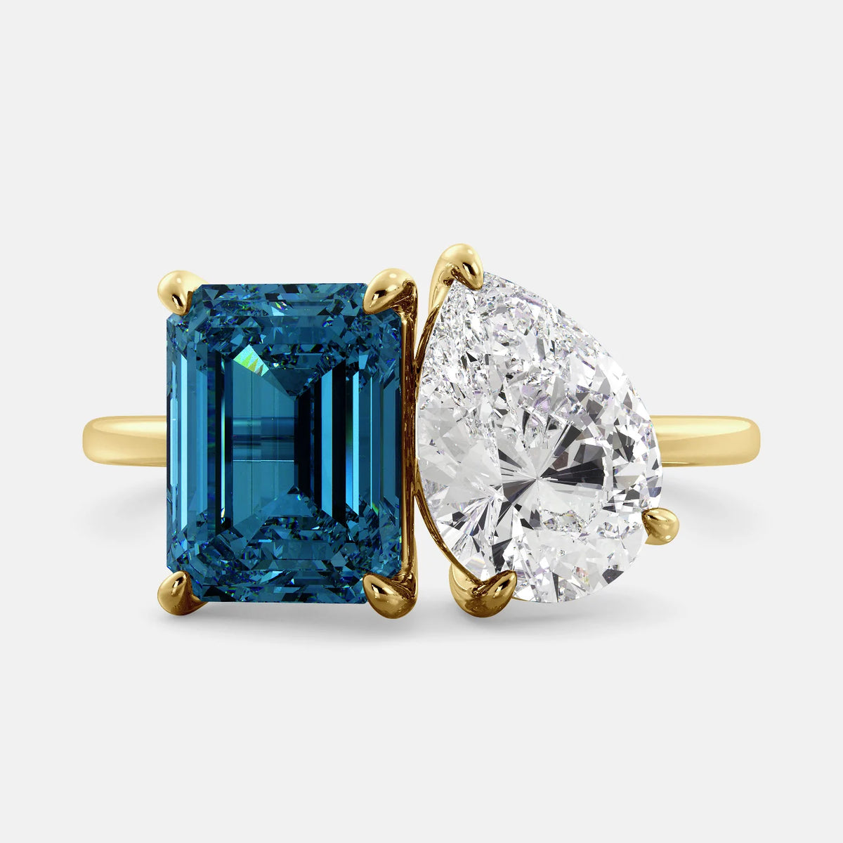A toi et moi ring with an emerald-cut London Blue Topaz and pear-cut gemstone. The emerald-cut morganite is set on the left of the ring, and the pear-cut gemstone is set on the right. The ring is made of recycled yellow gold and has a simple, elegant design. The pear-cut gemstone can be customized. **Here are some additional details about the image:** * The emerald-cut white London Blue Topaz is a birthstone for December. * The pear-cut gemstone can be customized to any stone of your choice.