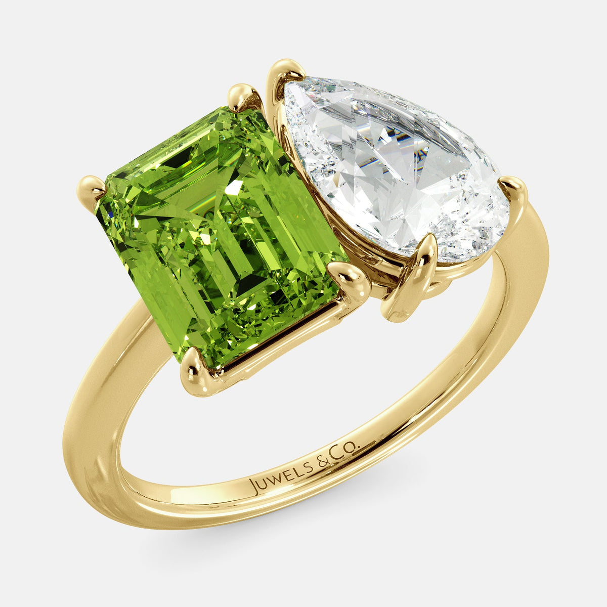A toi et moi ring with an emerald-cut Green Peridot and a pear-cut gemstone. The emerald-cut morganite is set on the left of the ring, and the pear-cut gemstone is set on the right. The ring is made of recycled yellow gold and has a simple, elegant design. The pear-cut gemstone can be customized. **Here are some additional details about the image:** * The emerald-cut white Green Peridot is a birthstone for August. * The pear-cut gemstone can be customized to any stone of your choice.