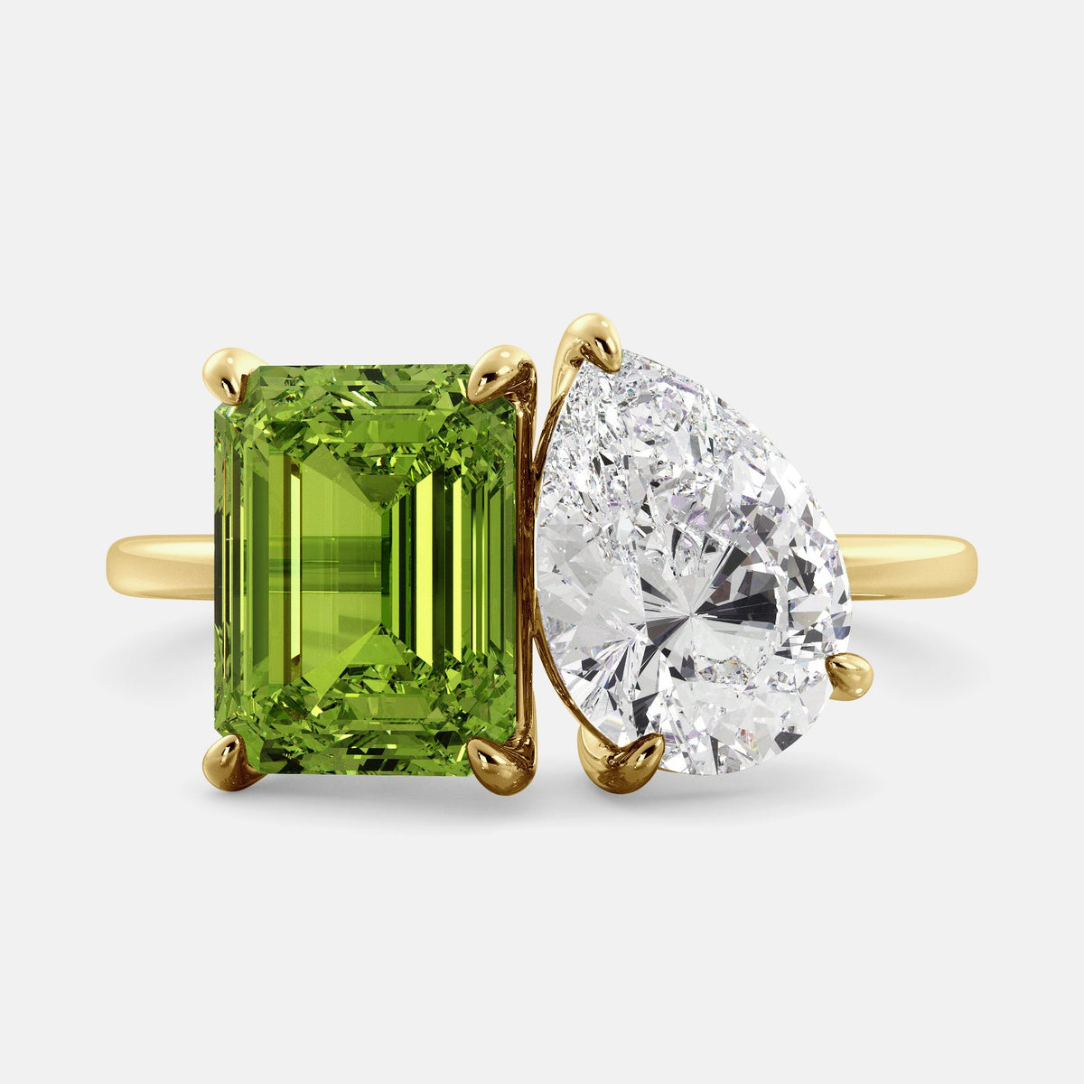 A toi et moi ring with an emerald-cut Green Peridot and a pear-cut gemstone. The emerald-cut morganite is set on the left of the ring, and the pear-cut gemstone is set on the right. The ring is made of recycled yellow gold and has a simple, elegant design. The pear-cut gemstone can be customized. **Here are some additional details about the image:** * The emerald-cut white Green Peridot is a birthstone for August. * The pear-cut gemstone can be customized to any stone of your choice.