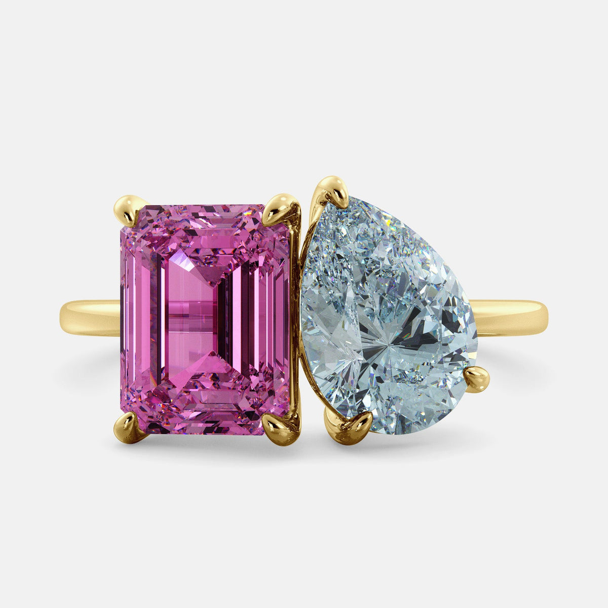 A toi et moi ring with an emerald-cut Pink Sapphire and pear-cut gemstone. The emerald-cut is set on the left of the ring, and the pear-cut gemstone is set on the right. The ring is made of recycled yellow gold and has a simple, elegant design. The pear-cut gemstone can be customized. **Here are some additional details about the image:** * The emerald-cut white Pink Sapphire is a birthstone for October. * The pear-cut gemstone can be customized to any stone of your choice.