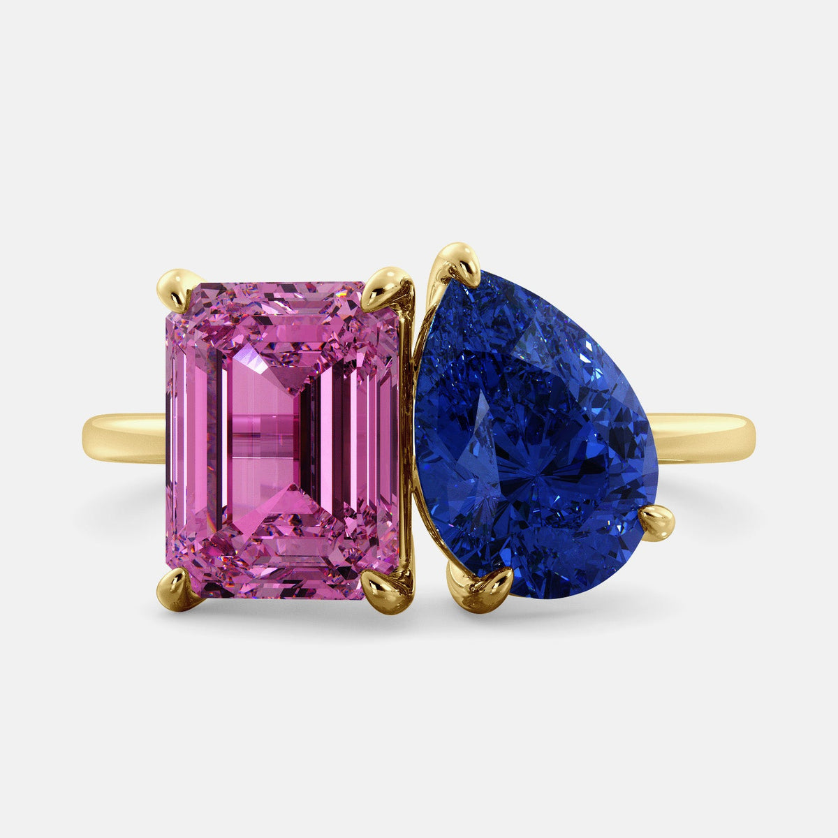 A toi et moi ring with an emerald-cut Pink Sapphire and pear-cut gemstone. The emerald-cut is set on the left of the ring, and the pear-cut gemstone is set on the right. The ring is made of recycled yellow gold and has a simple, elegant design. The pear-cut gemstone can be customized. **Here are some additional details about the image:** * The emerald-cut white Pink Sapphire is a birthstone for October. * The pear-cut gemstone can be customized to any stone of your choice.