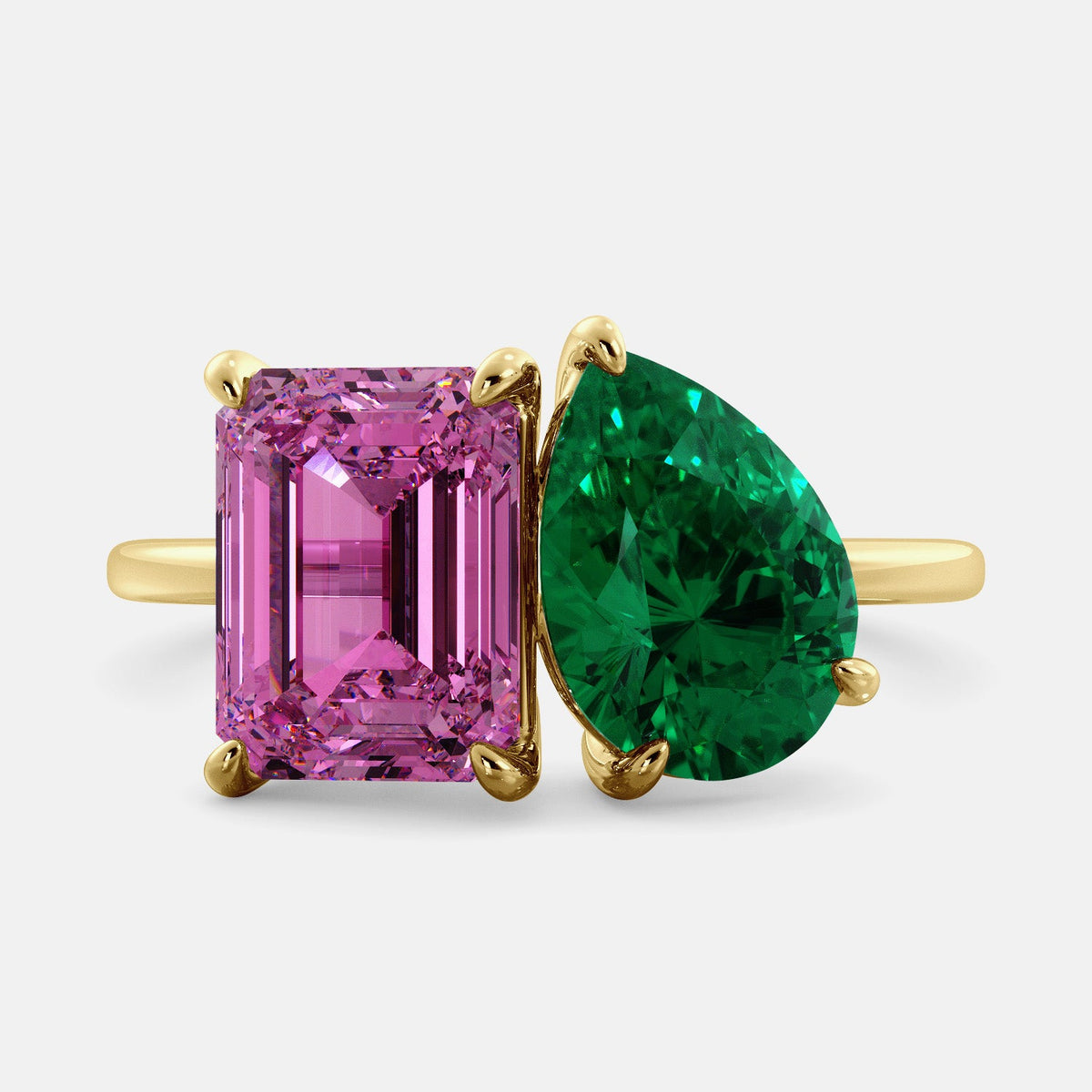 A toi et moi ring with an emerald-cut Pink Sapphire and pear-cut gemstone. The emerald-cut is set on the left of the ring, and the pear-cut gemstone is set on the right. The ring is made of recycled yellow gold and has a simple, elegant design. The pear-cut gemstone can be customized. **Here are some additional details about the image:** * The emerald-cut white Pink Sapphire is a birthstone for October. * The pear-cut gemstone can be customized to any stone of your choice.