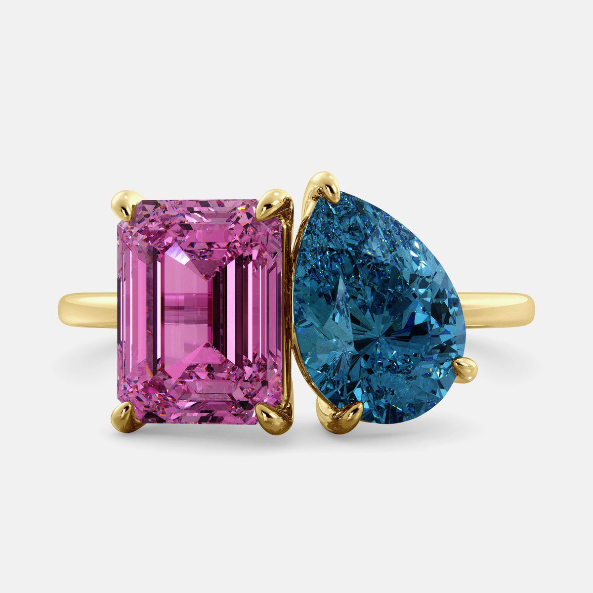 A toi et moi ring with an emerald-cut Pink Sapphire and pear-cut gemstone. The emerald-cut is set on the left of the ring, and the pear-cut gemstone is set on the right. The ring is made of recycled yellow gold and has a simple, elegant design. The pear-cut gemstone can be customized. **Here are some additional details about the image:** * The emerald-cut white Pink Sapphire is a birthstone for October. * The pear-cut gemstone can be customized to any stone of your choice.