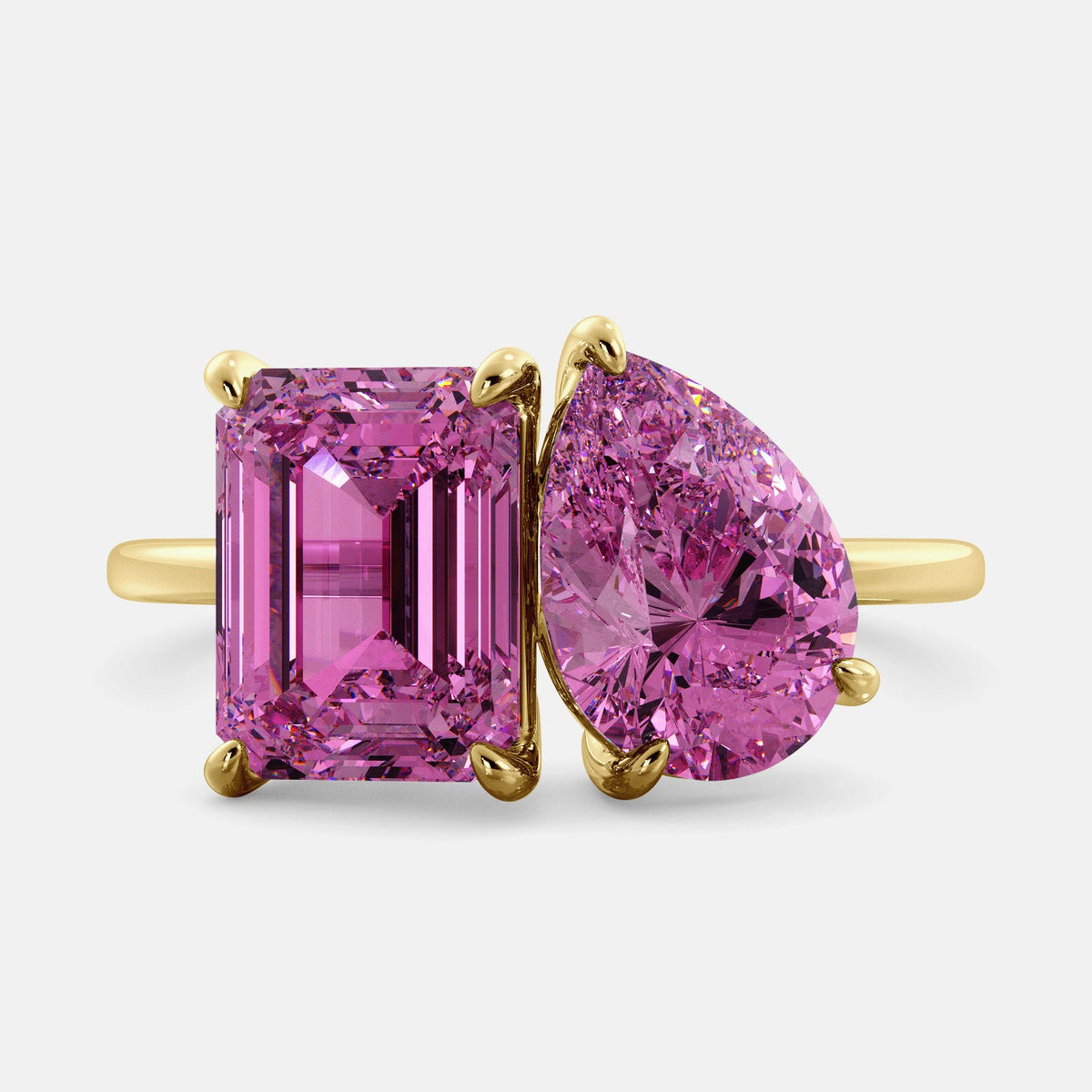 A toi et moi ring with an emerald-cut Pink Sapphire and pear-cut gemstone. The emerald-cut is set on the left of the ring, and the pear-cut gemstone is set on the right. The ring is made of recycled yellow gold and has a simple, elegant design. The pear-cut gemstone can be customized. **Here are some additional details about the image:** * The emerald-cut white Pink Sapphire is a birthstone for October. * The pear-cut gemstone can be customized to any stone of your choice.