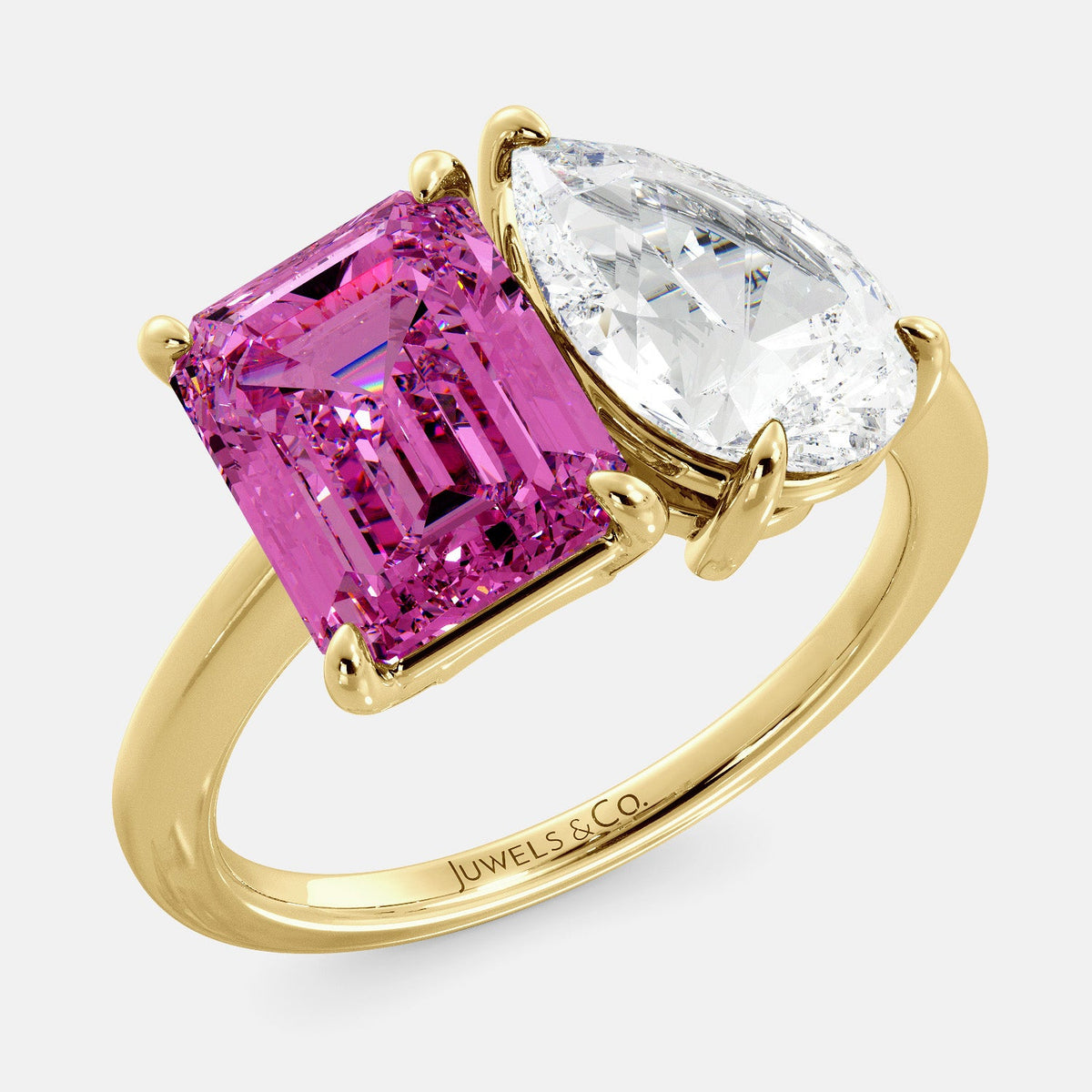 A toi et moi ring with an emerald-cut Pink Sapphire and pear-cut gemstone. The emerald-cut is set on the left of the ring, and the pear-cut gemstone is set on the right. The ring is made of recycled yellow gold and has a simple, elegant design. The pear-cut gemstone can be customized. **Here are some additional details about the image:** * The emerald-cut white Pink Sapphire is a birthstone for October. * The pear-cut gemstone can be customized to any stone of your choice.
