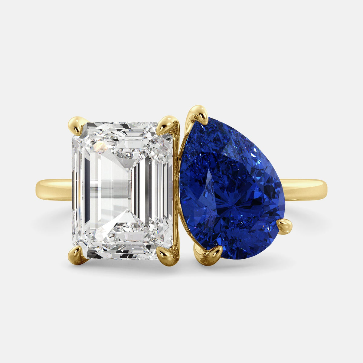 A toi et moi ring with an emerald-cut white topaz and a pear-cut gemstone. The emerald-cut morganite is set on the left of the ring, and the pear-cut gemstone is set on the right. The ring is made of recycled yellow gold and has a simple, elegant design. The pear-cut gemstone can be customized. **Here are some additional details about the image:** * The emerald-cut white topaz is a birthstone for April. * The pear-cut gemstone can be customized to any stone of your choice.