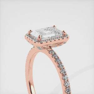 This image shows a stunning emerald halo lab-grown diamond ring with pavé on a rose gold band. The ring features a 1.5-carat emerald-cut lab-grown diamond in the center, surrounded by a halo of smaller lab-grown diamonds. The ring is made of 14k rose gold and is available in a variety of sizes.