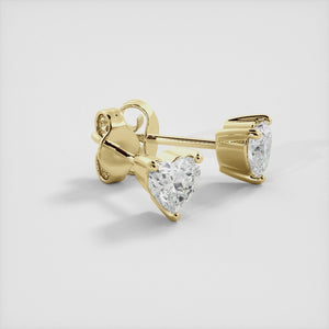 A close-up of a pair of heart-shaped diamond stud earrings in recycled yellow gold. Each earring is set with a single heart shape diamond in the center. The earrings are made of recycled yellow gold and have a simple, elegant design. The diamonds are sparkling and reflect light beautifully. The earrings are a perfect gift for a loved one or a special occasion.