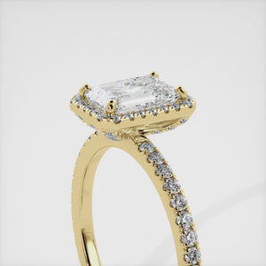 This image shows a stunning emerald halo lab-grown diamond ring with pavé on a yellow gold band. The ring features a 1.5-carat emerald-cut lab-grown diamond in the center, surrounded by a halo of smaller lab-grown diamonds. The ring is made of 14k yellow gold and is available in a variety of sizes.