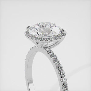 This image shows a beautiful round halo lab-diamond ring with pavé on a white gold band. The ring features a round brilliant-cut lab diamond in the center, surrounded by a halo of smaller diamonds. The band is pavé-set with smaller diamonds, creating a sparkling and elegant look. The ring is made of 14k white gold and is available in a variety of sizes.